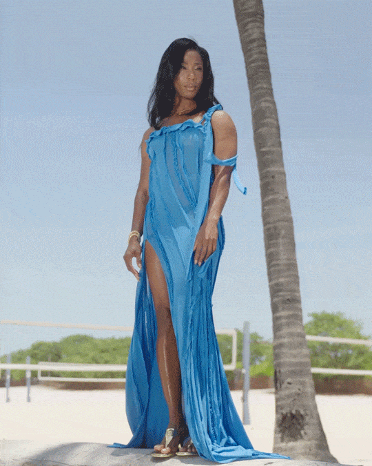 Shelly-Anna Fraser-Pryce wearing a blue flowy dress standing next to a palm tree