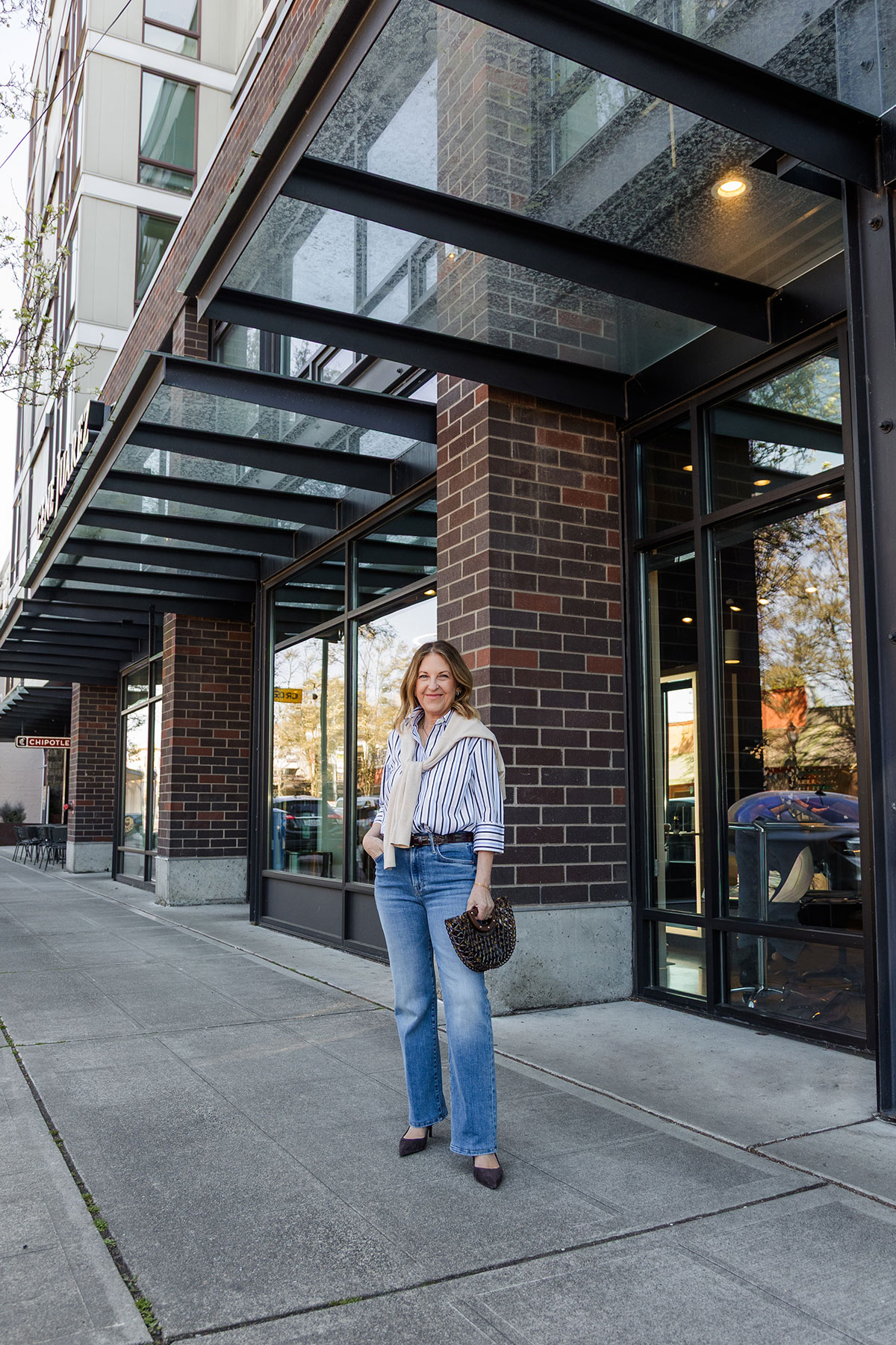 A former VIP Nordstrom stylist wearing a striped button down, jeans, and slingbacks.