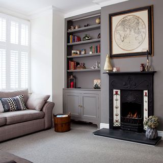 grey living room with grey carpet flooring and a fire place next to a wall-mounted book shelf and a grey striped sofa with pillows