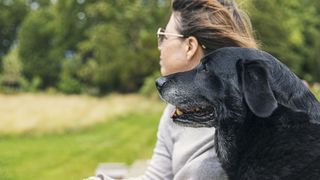 a woman and her senior black lab sit together in a park