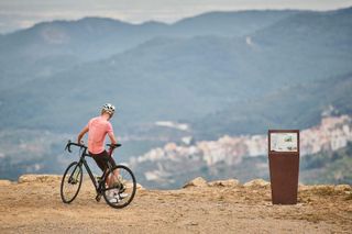 A cyclist leans against his bike at the top of a climb