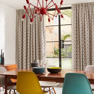 A dining room with retro furniture, a statement red pendant light and geometric print curtains