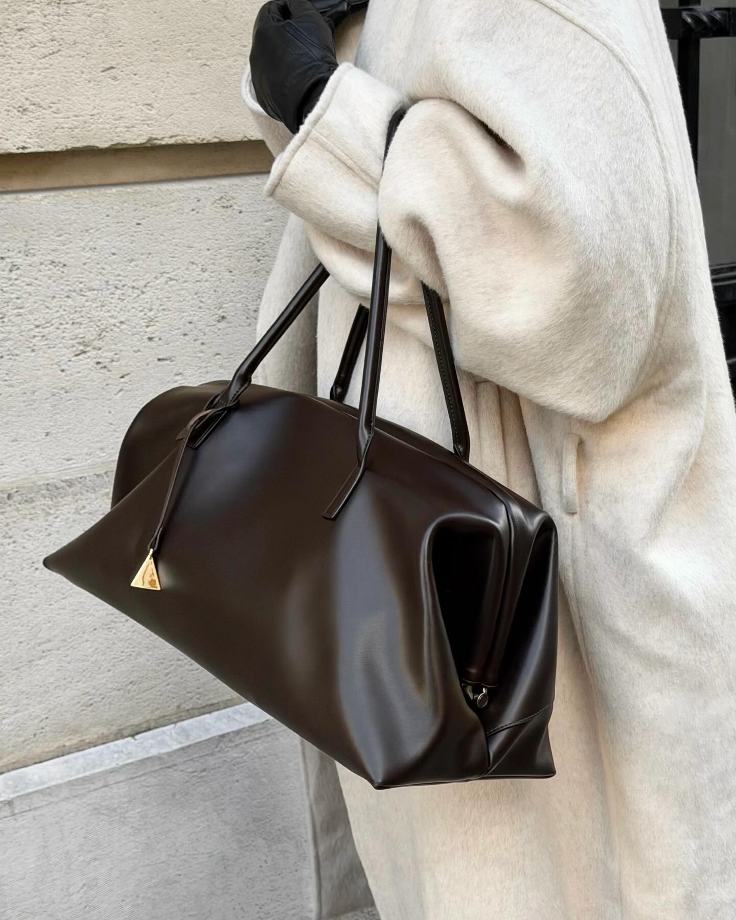 A model in a white wool coat holds Verafied's The Club Bag in chocolate brown.