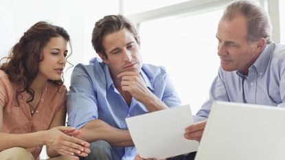 A couple sits at a desk with an an accountant going over paperwork.