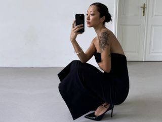 Model taking a mirror selfie wearing a black strapless Zara dress and black heels.