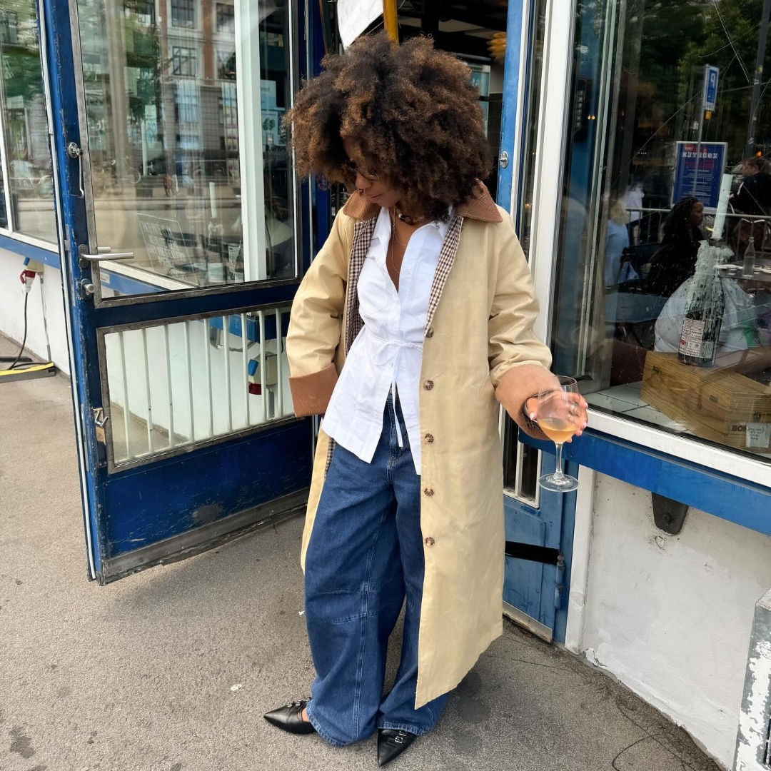 Amaka Hamelijnck wears an ovresized trench coat, whit top, and wide jeans in Copenhagen, Denmark