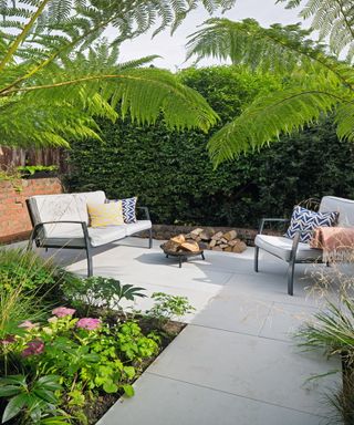 A modern grey patio area with lush, colourful planting and trees around it