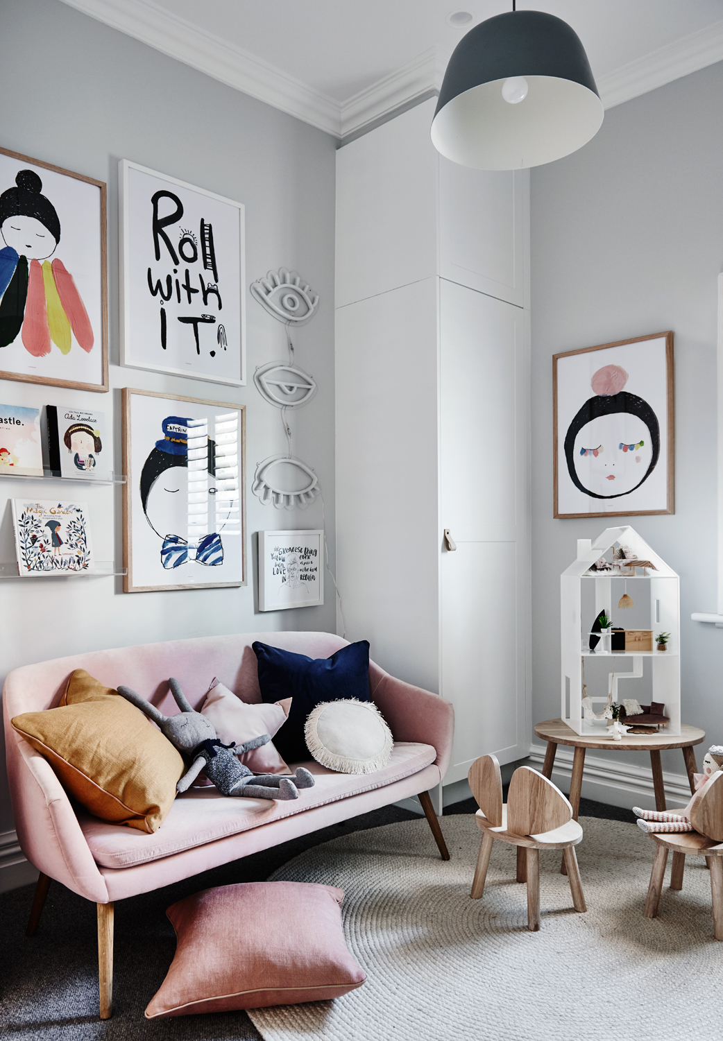 Fun gallery wall in small living room with pink couch, mustard and black cushion assortment