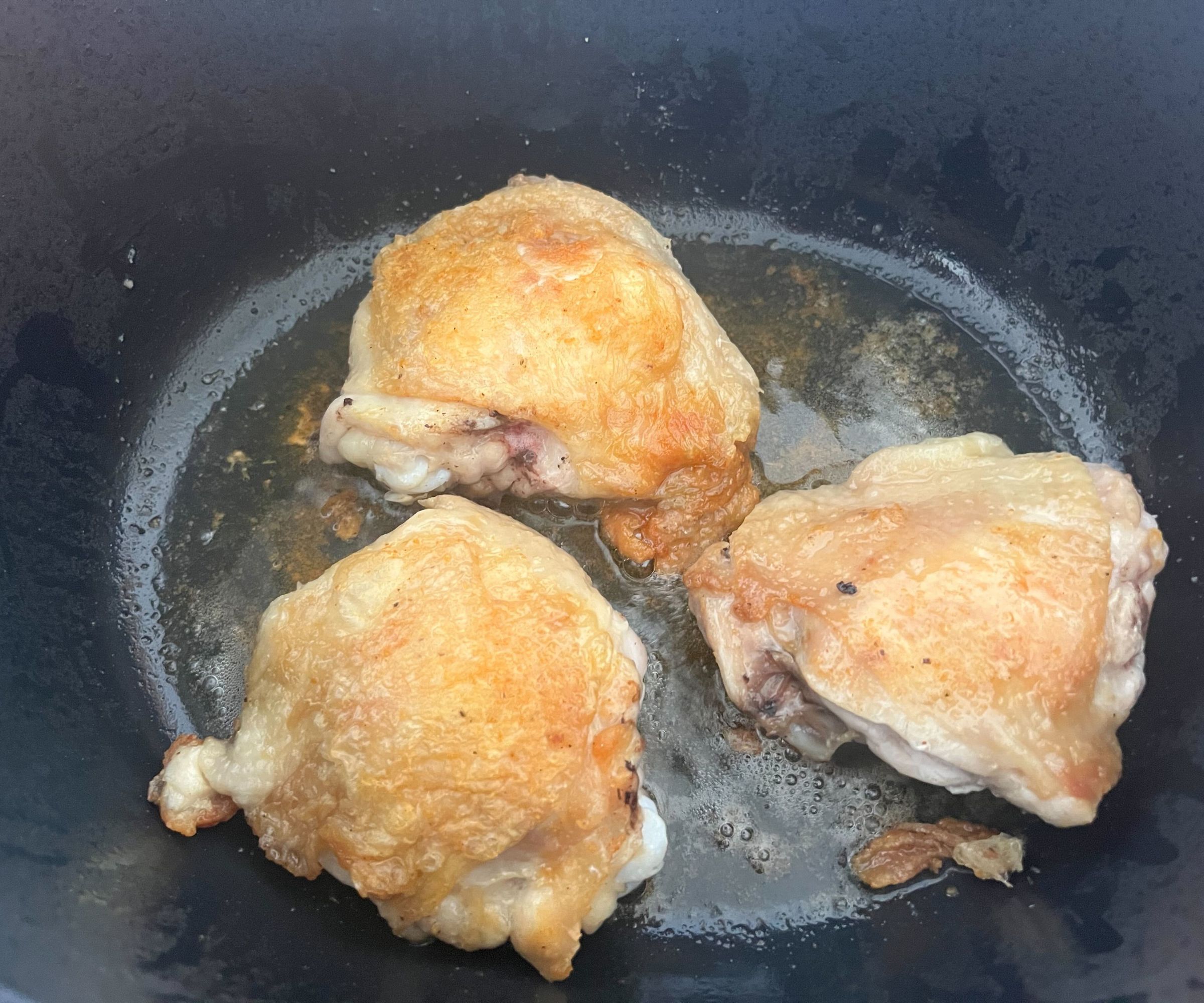 Golden skin on cooking chicken thighs in a black Dutch oven
