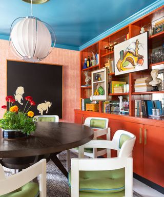 dining room with bright red cabinets, bright blue ceiling and green dining chairs around round wooden table