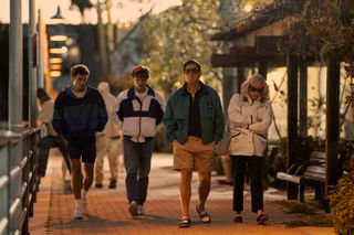 Cooper Koch as Erik Menendez, Nicholas Chavez as Lyle Menendez, Javier Bardem as Jose Menendez, and Chloë Sevigny as Kitty Menendez, walking down a brick-lined street, in episode 204 of Monsters: The Lyle And Erik Menendez Story.