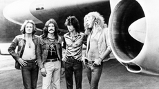 Led Zeppelin stand beneath the wings of their plane.