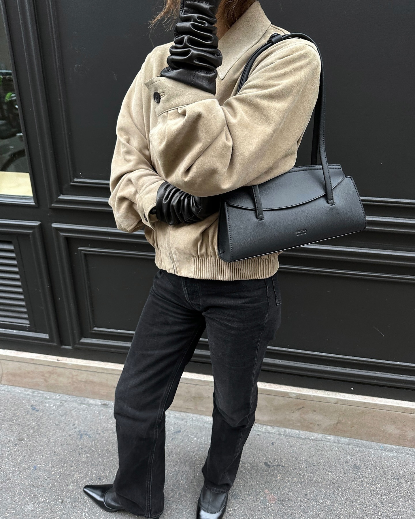 @sarahrosepalm wearing a tan suede jacket, black jeans, and a black bag.