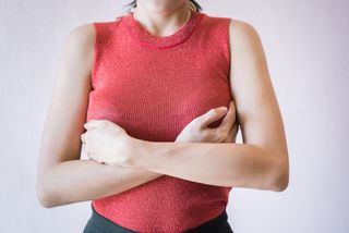 Midsection Of Woman Touching Breast While Standing Against White Background