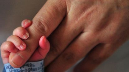 A newborn baby holds onto his mother's finger 