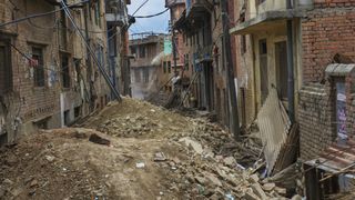 Khokana village in Kathmandu, Nepal, after a damaging earthquake. Here we see a narrow street filled with rubble and lined with damaged buildings and electrical wires.