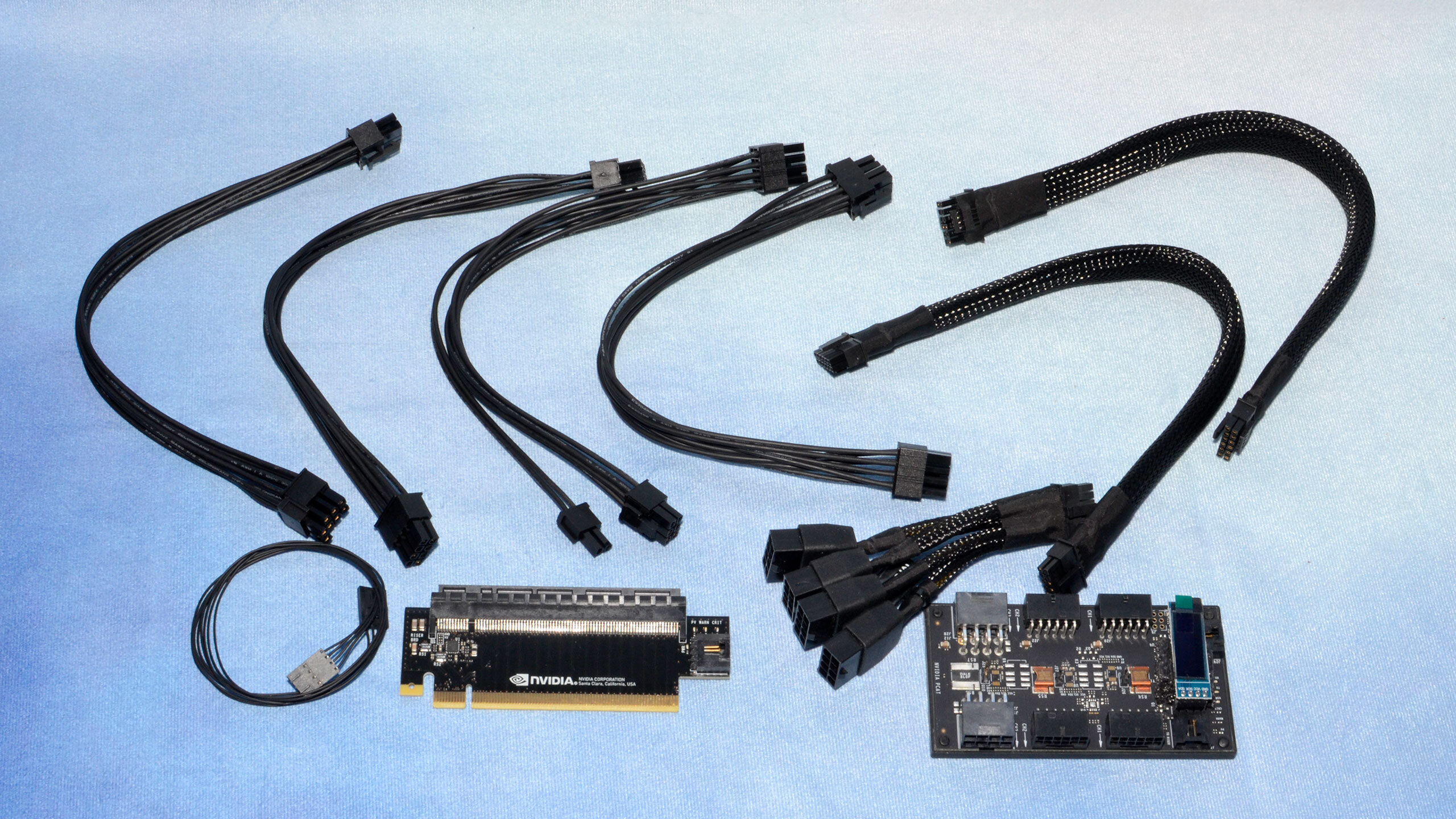 An Nvidia PCAT device with accessories such as cables and a breakout PCB on a blue background.