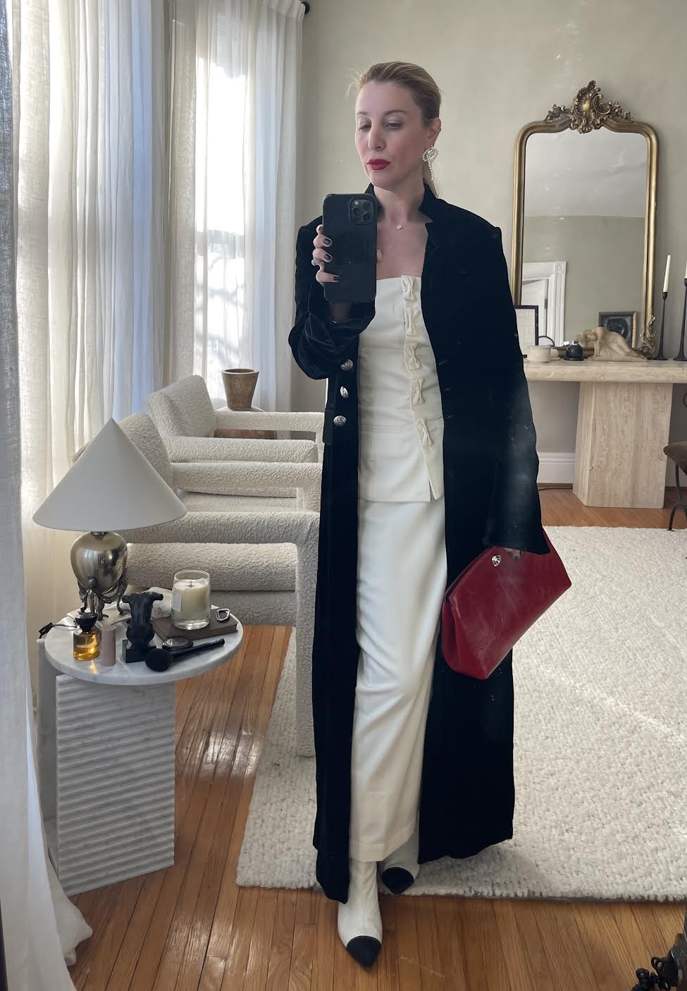 Kerry Pieri wearing a white top, white skirt, black velvet coat, white and black captoe boots, and a red clutch