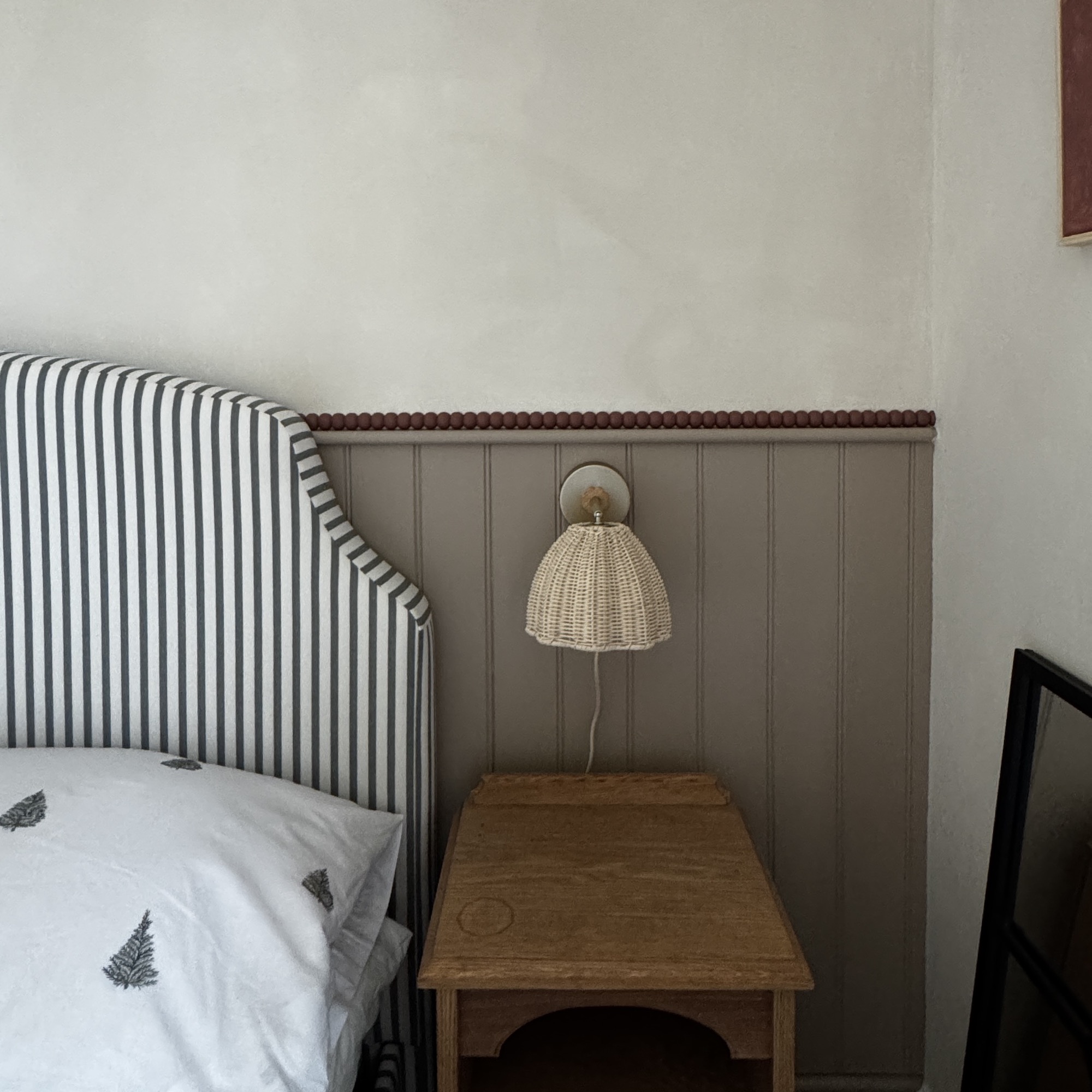 bedroom with beside table, rattan wall lamp and striped headboard