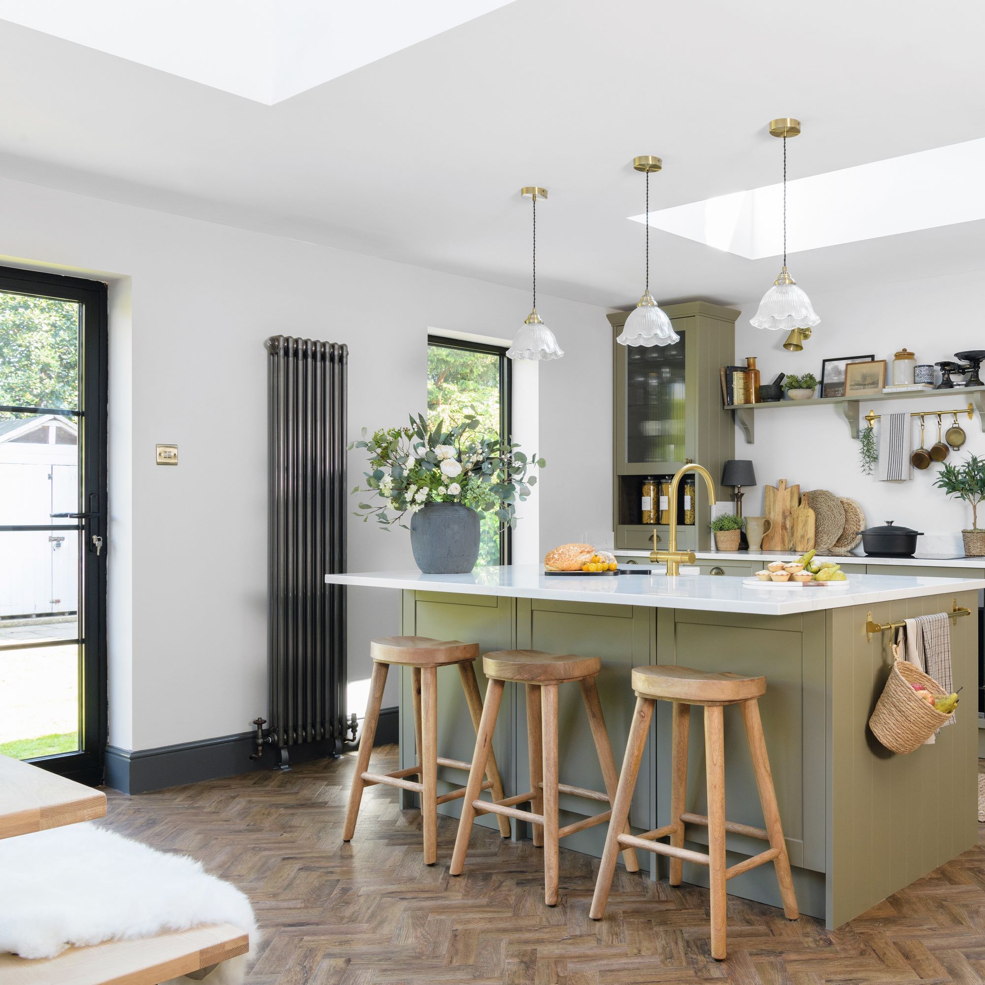 olive green kitchen island with wooden stools and potted flowers