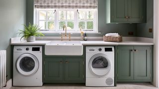 utility room with back wall featuring window, roman blind, butlers sink, green base units, green wall cabinets and laundry appliances