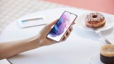 Woman's hand holding Samsung Galaxy s21 5G phone over a table containing a cronut on a plate