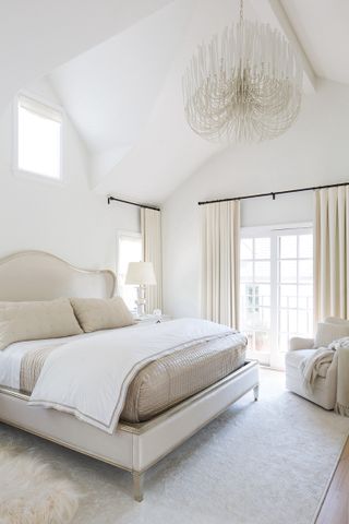 A bedroom in neutral cream tones, with large window and cream curtains