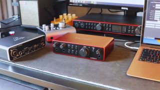 A Focusrite Scarlett 2i2 on a desk with various audio interfaces in the background