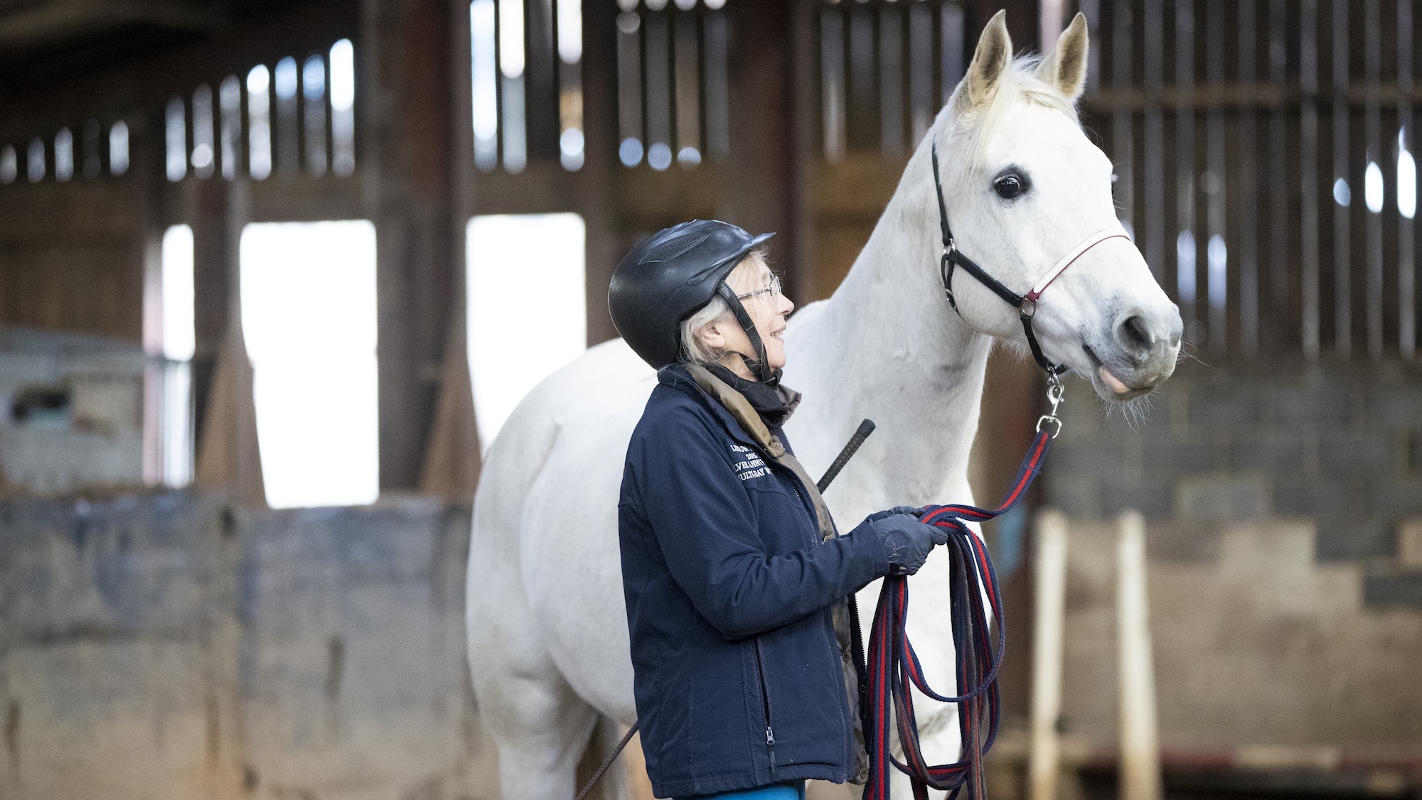 Lady holding grey horse on lunge line.
