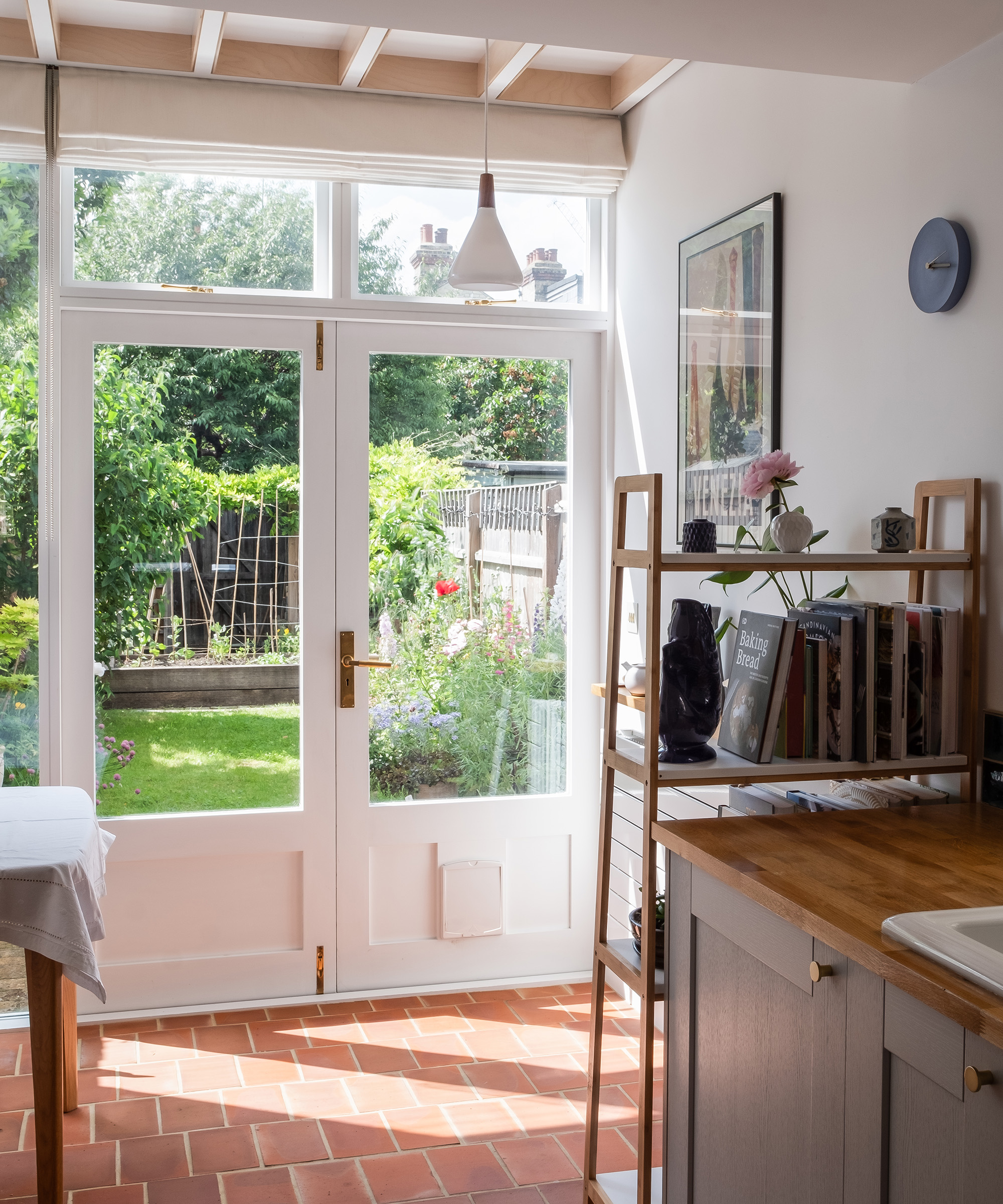 Rear french doors looking out to a garden. There is terracotta flooring in the kitchen