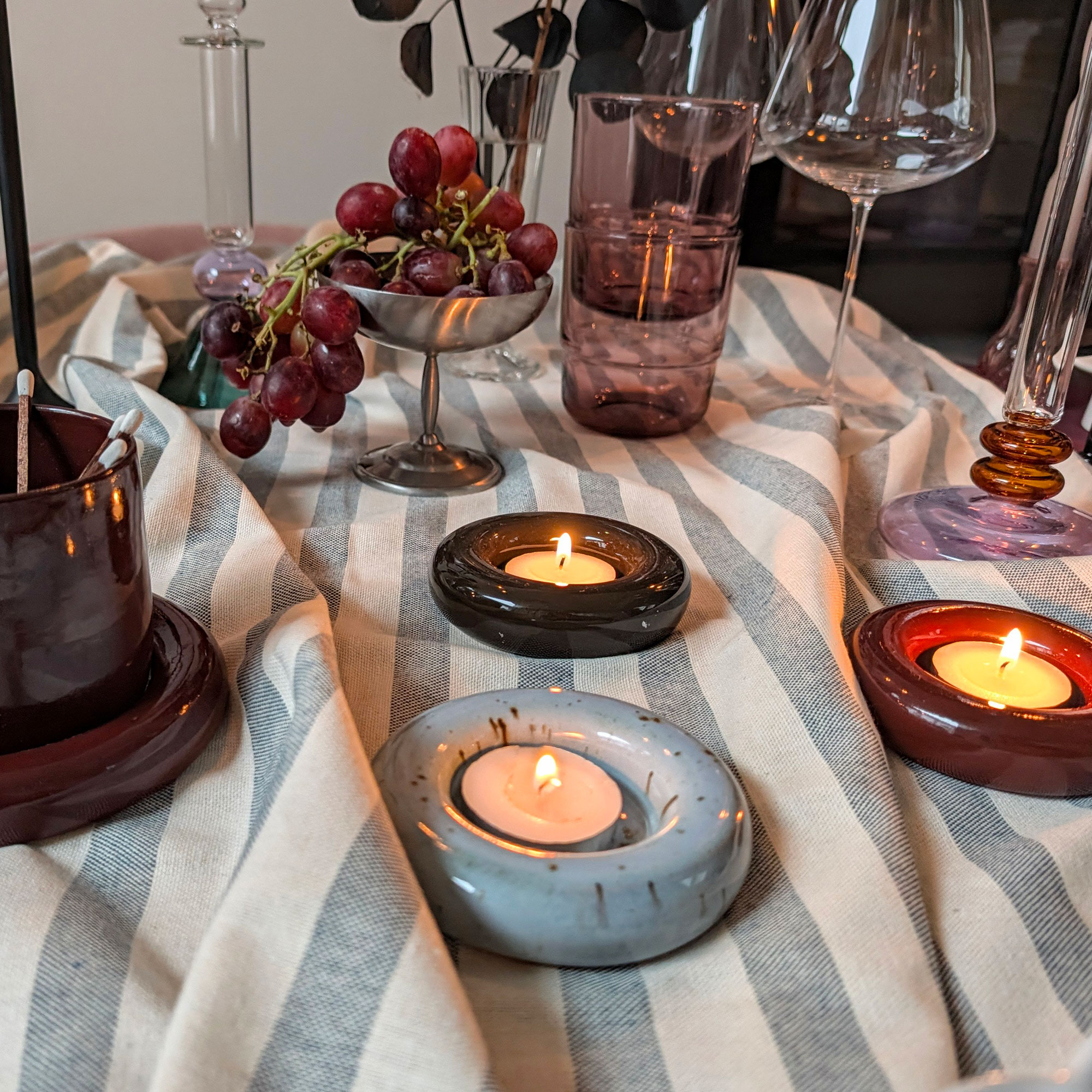 Table with striped tablecloth, three round ceramic tealight holders, silver coupe and various glassware