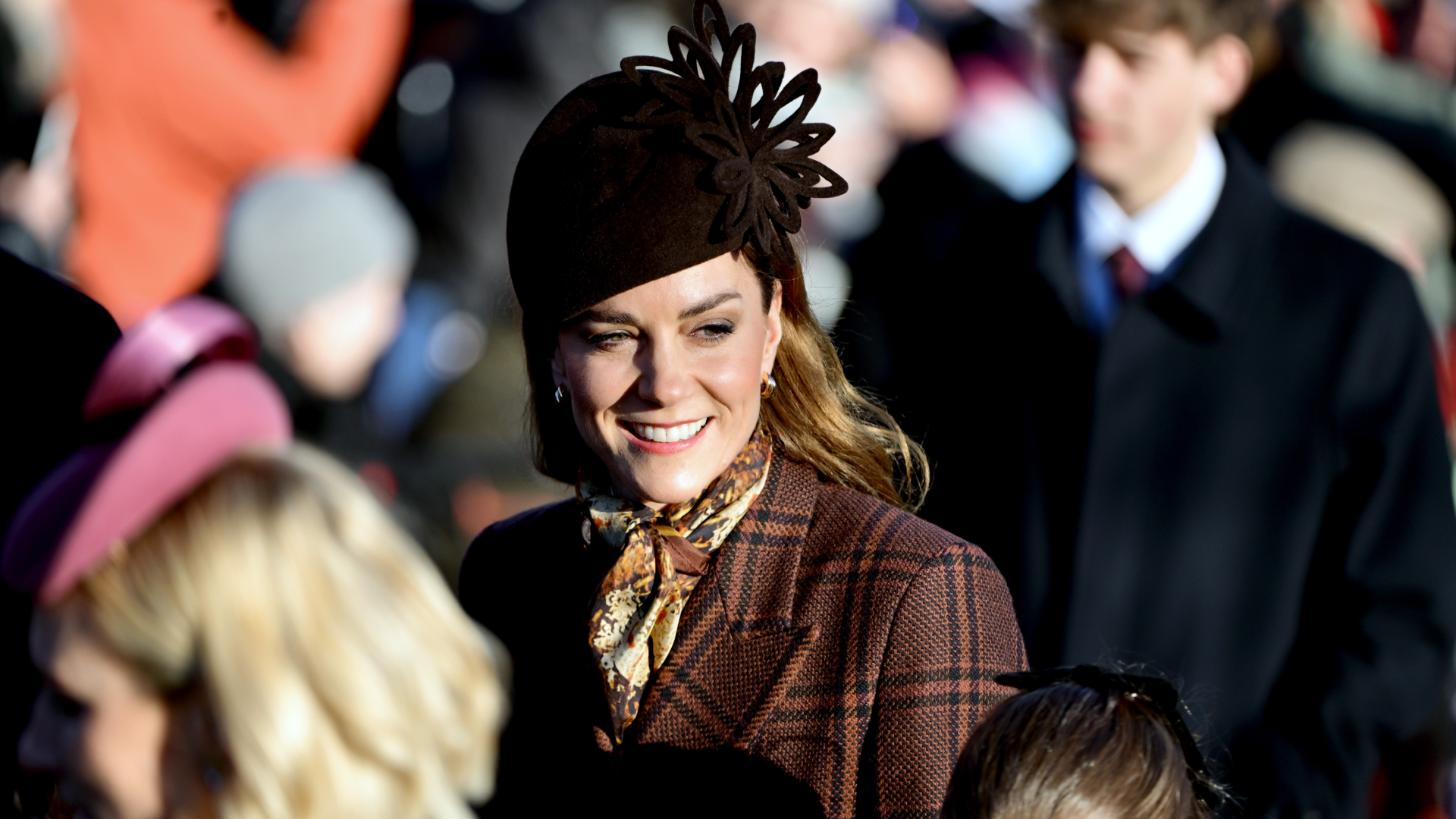Princess Kate smiling, wearing a brown plaid coat and brown hat