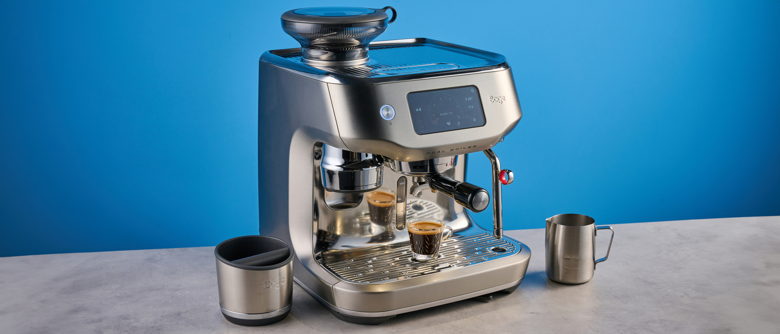 the breville oracle dual boiler / sage oracle dual boiler in stainless steel, showing its touchscreen, steam wand, built in grinder, and espresso shots