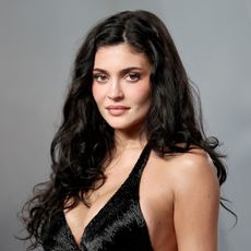 a white woman with long, dark hair photographed in front of a gray backdrop