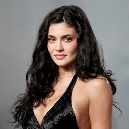 a white woman with long, dark hair photographed in front of a gray backdrop