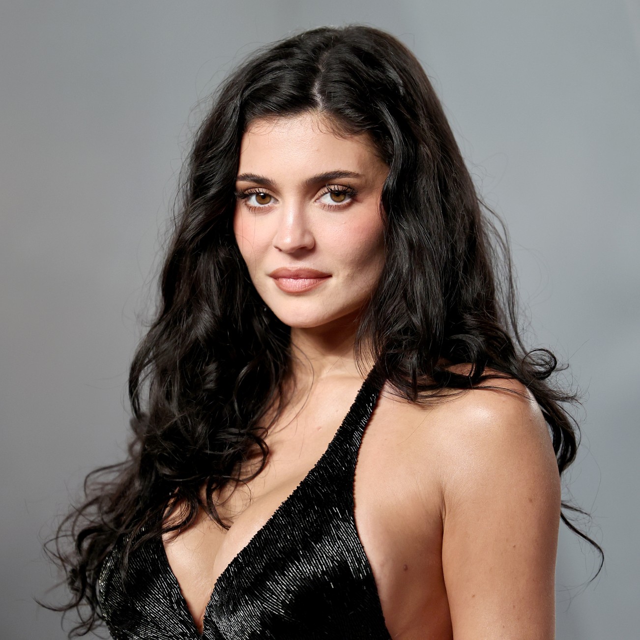 a white woman with long, dark hair photographed in front of a gray backdrop