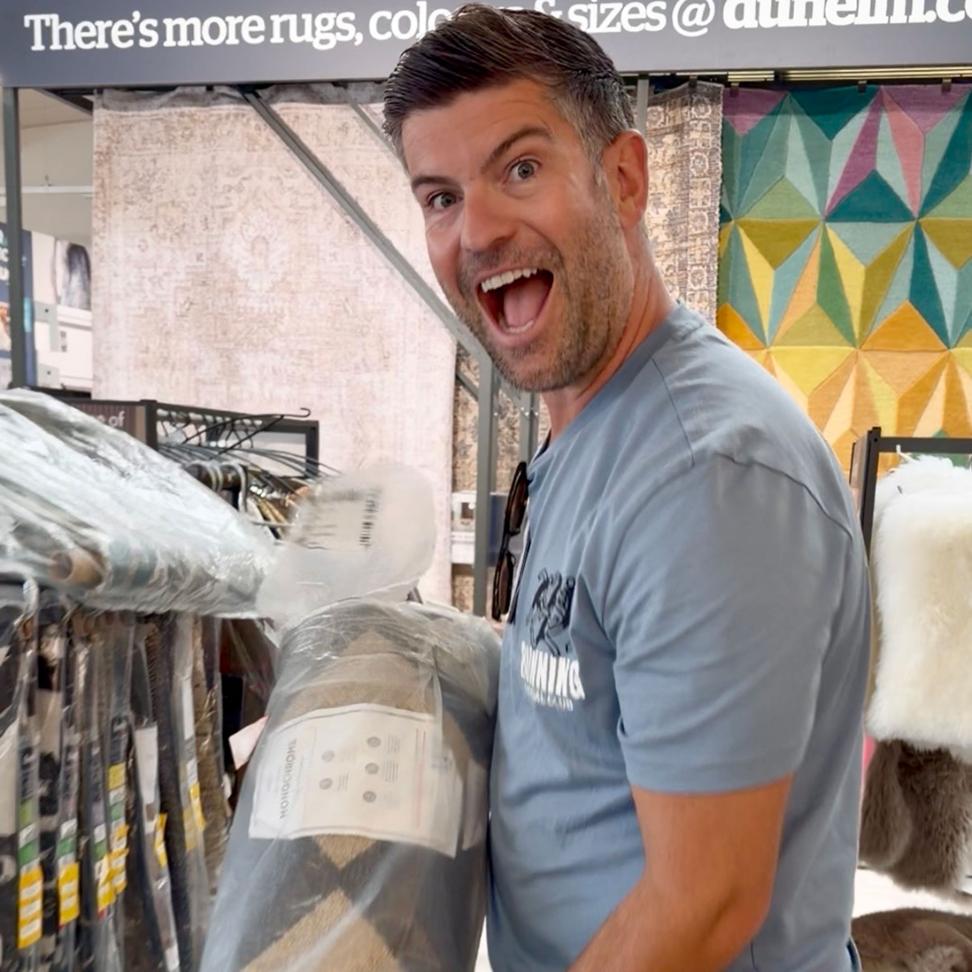 Man smiling while holding rug inside shop