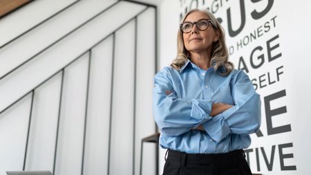 mature business woman in the office stands with her arms crossed on her chest in a blue shirt.