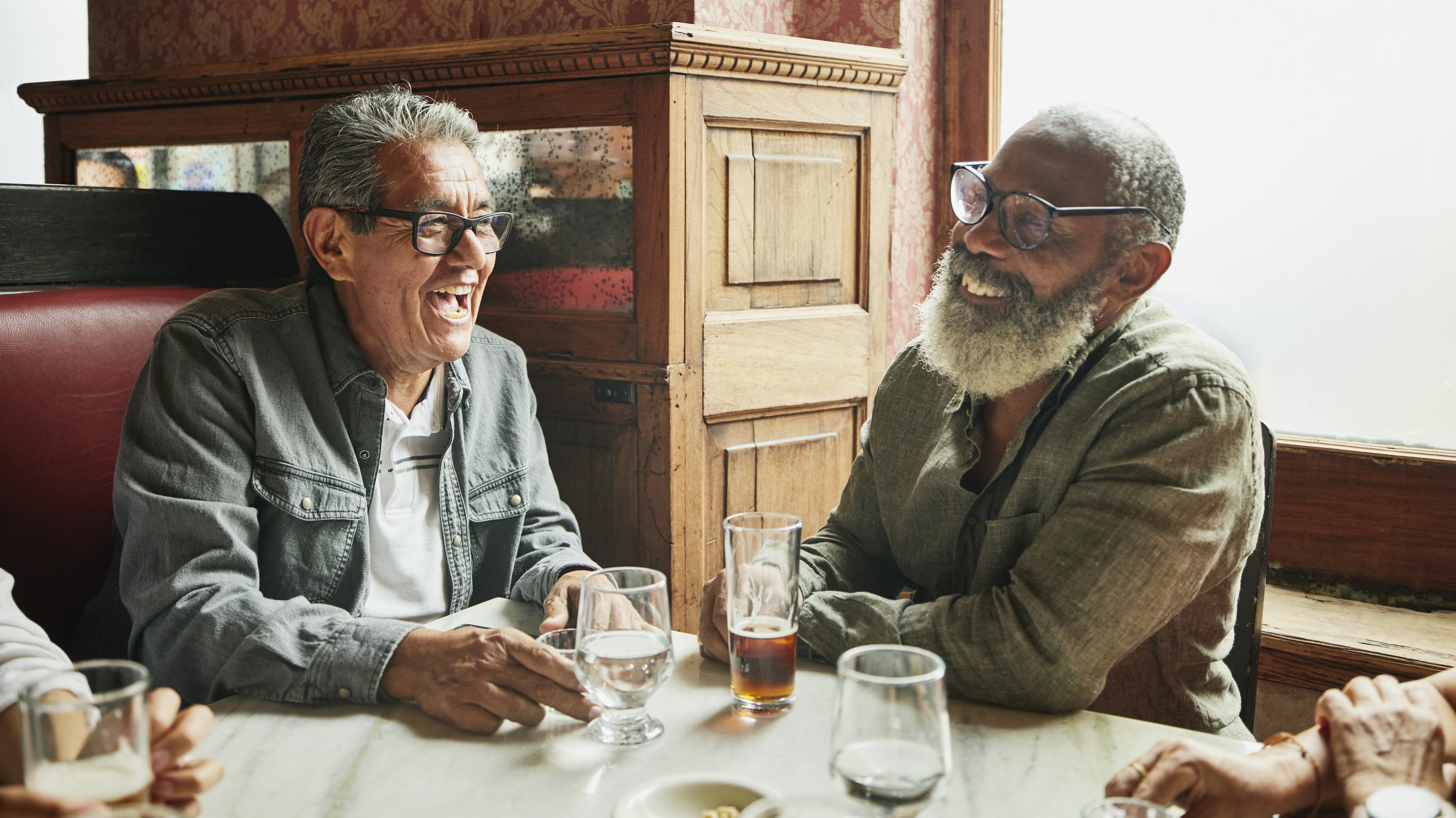 Two older men laugh together in a restaurant.