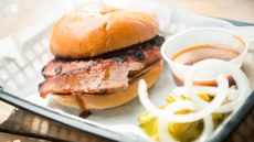 A plate of a Gatlin's Barbecue brisket sandwich with a side of barbecue sauce and onions