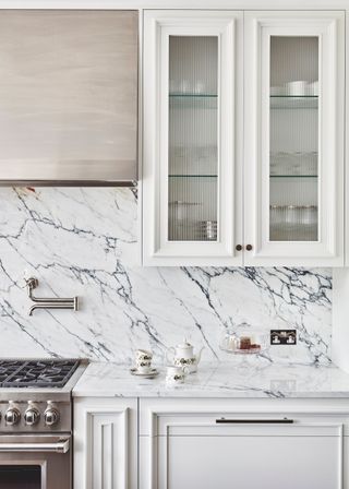 White fluted glass kitchen cabinets with glass inserts in a marbled kitchen.