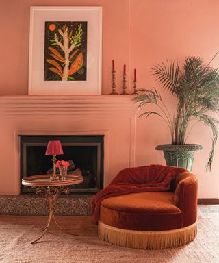 Color drenched living room in coral, matching mantel, artwork and candles on mantel, jute rug, fringed orange armchair, gold vintage side table