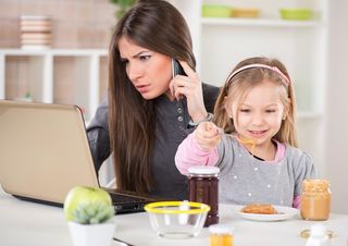 A mom works on her computer and talks on her phone while her daughter sits on her lap.