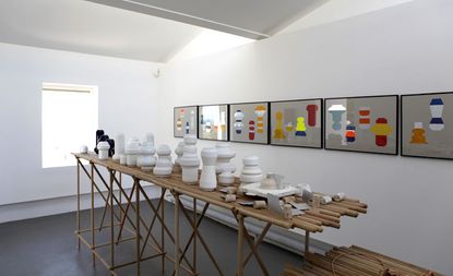 White ceramic art display on wooden tables, against a white wall with wall art hanging