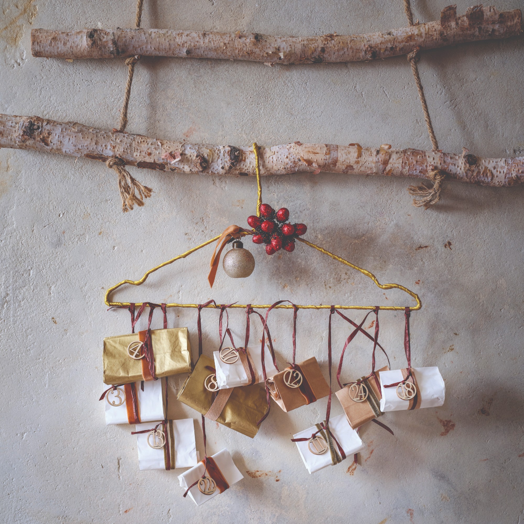 A DIY advent calendar made with a hangers, ribbon and little numbered paper bags hanging from two birch tree branches
