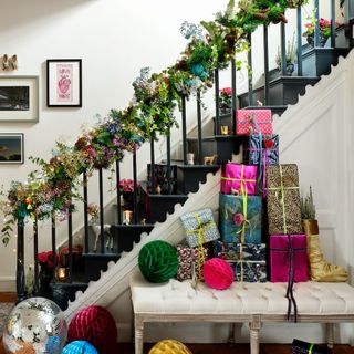 Black staircase decorated with green garland and hydrangea heads next to white bench filled with wrapped gifts