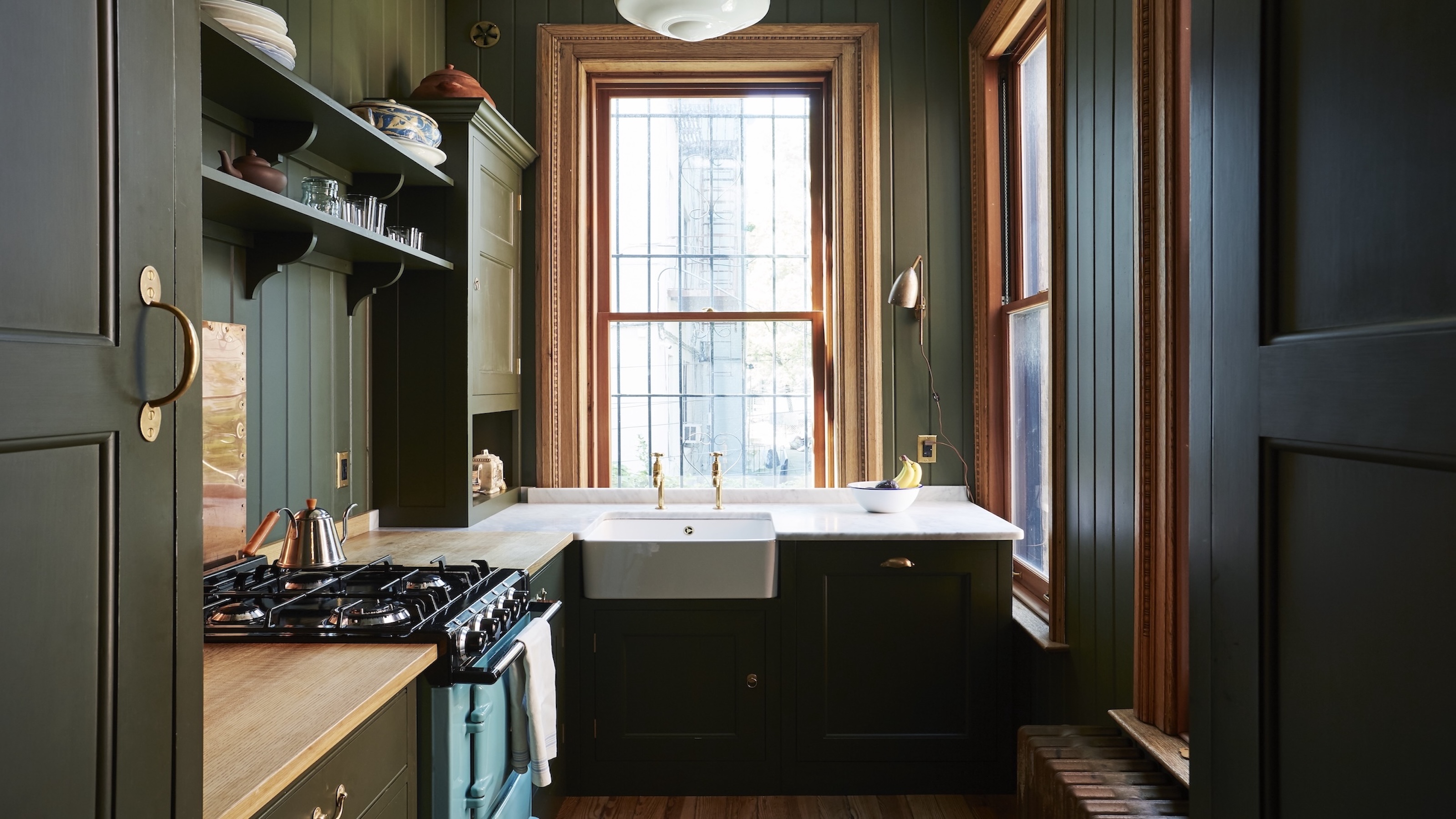 A traditional dark green kitchen with tongue and groove panelling, a wall light and brass hardware