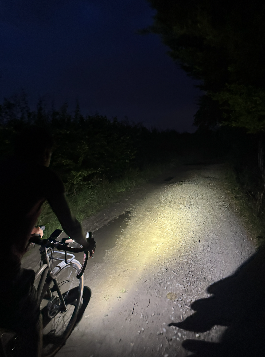 A dark gravel path with a bike riding it, lighting up beneath the 600 lumens of the Magicshine ALLTY 1200