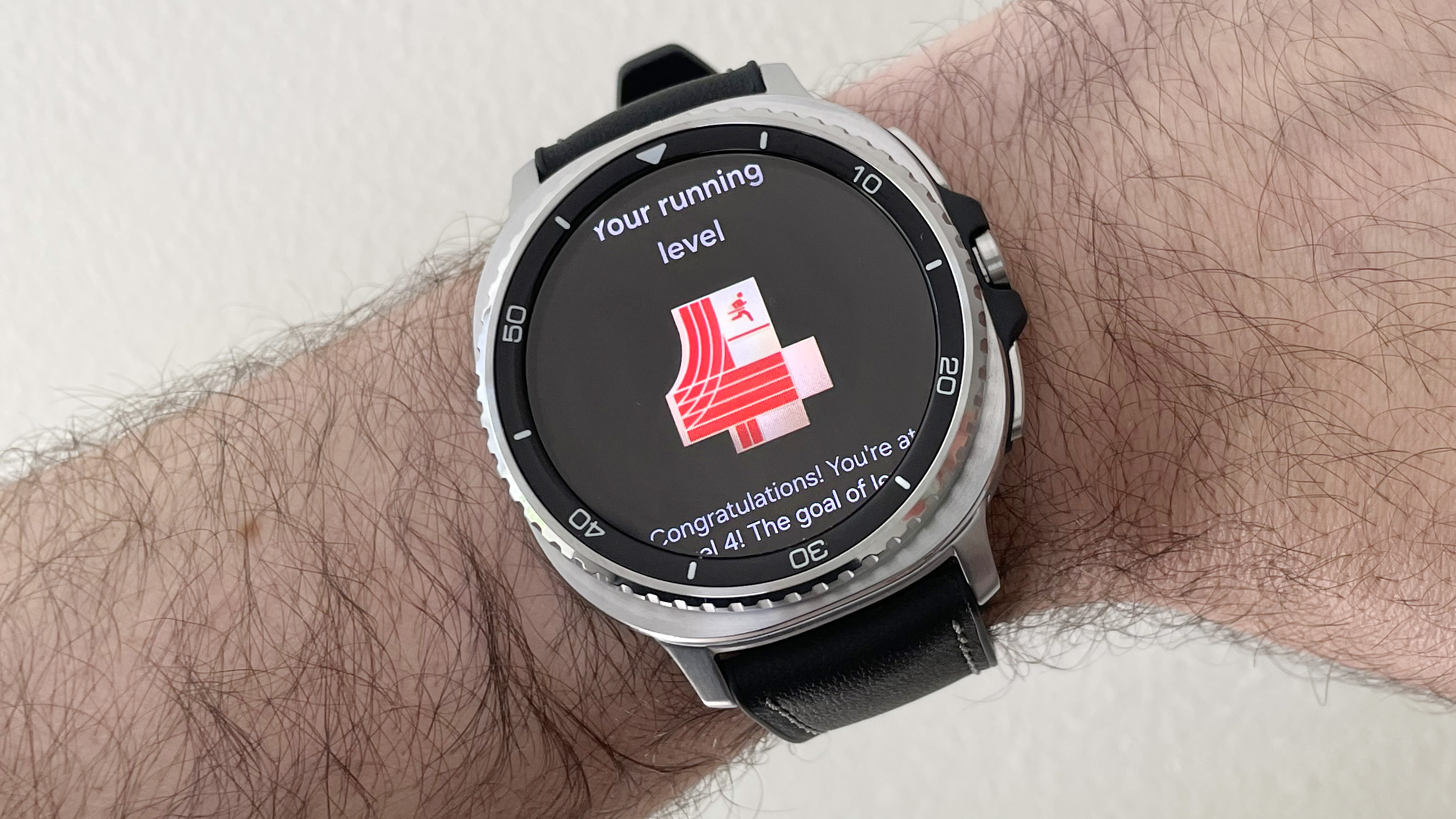 Close-up of the Samsung Galaxy Watch 8 Classic in silver on a black strap showing the Running Coach feature with a score of "4" after the trial test