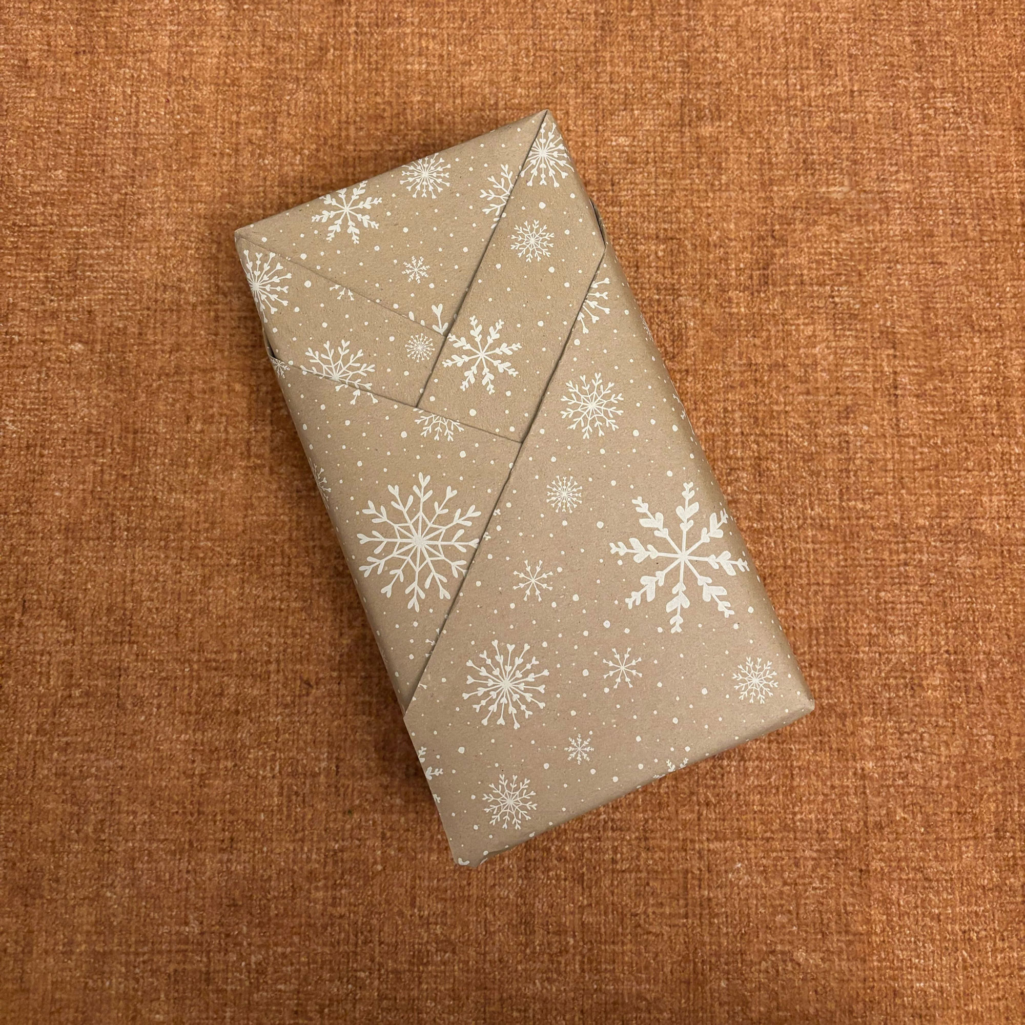 A rectangular box wrapped in brown paper with a white snowflake print on it